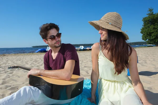Молодой человек с гитарой и подругой на пляже — стоковое фото