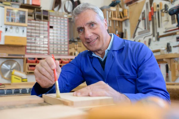 Porträt eines glücklichen Senior-Tischlers, der Holz in der Werkstatt lackiert — Stockfoto