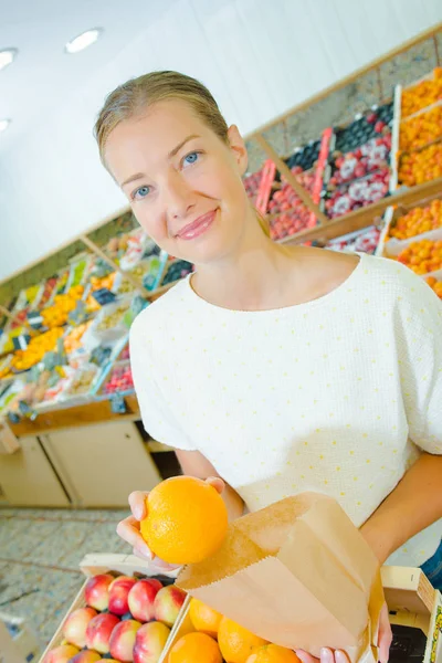 Jovem mulher colocando uma laranja em um saco de papel — Fotografia de Stock