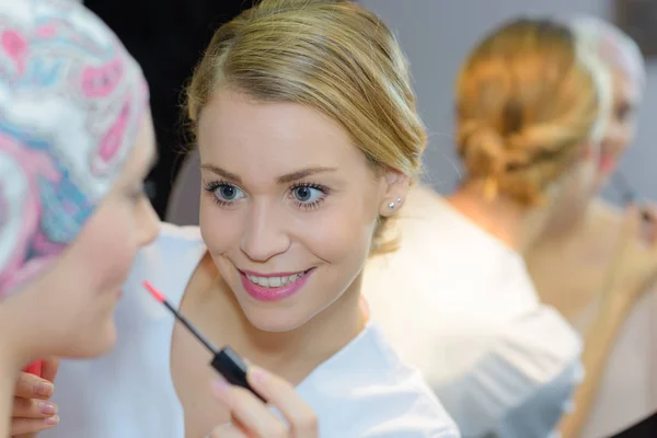 Kosmetikerin trägt Lipgloss auf Frau auf — Stockfoto