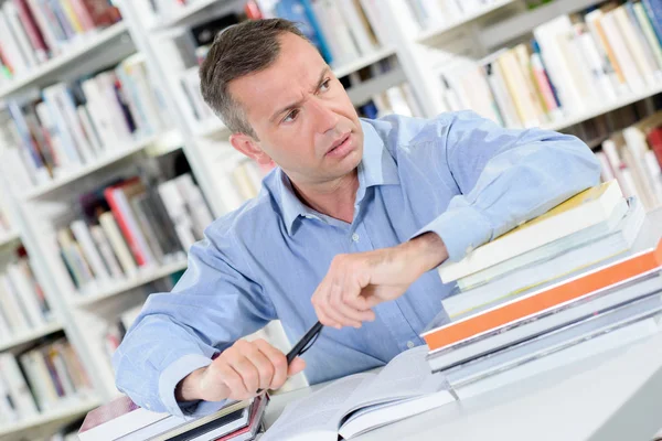 Homme assis à table à la bibliothèque, fronçant les sourcils — Photo