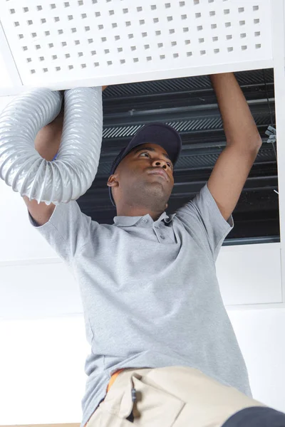 Giovane elettricista maschio africano sulla scala di ventilazione raccordo — Foto Stock