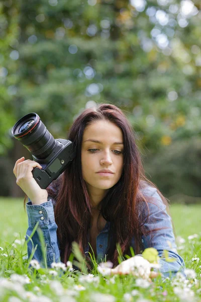 Jovem fotógrafo mulher com câmera deitar-se na grama — Fotografia de Stock