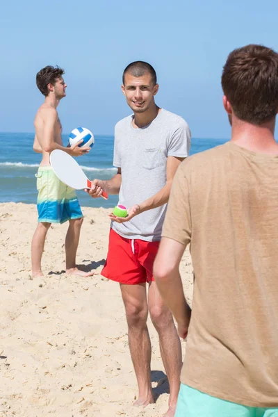 Vrolijke happy vrienden ontspannen aan het strand en spelen met rackets — Stockfoto