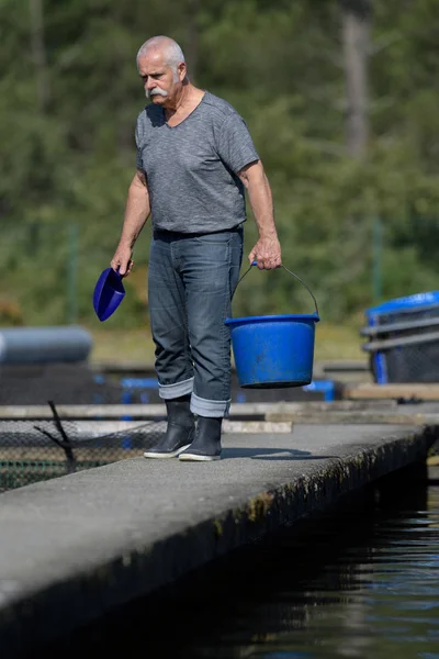 Gammal man fiskodling arbetare bär en hink — Stockfoto