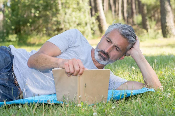 Man lingsitting in the grass reading a book — стоковое фото