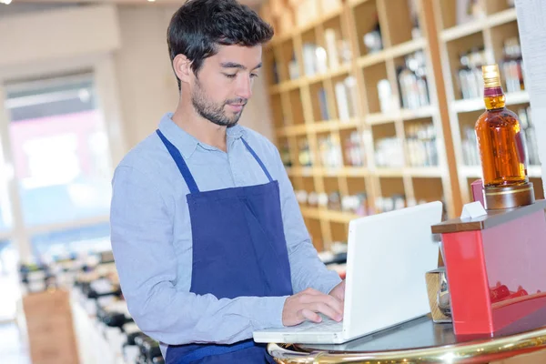Wine shop assistant checking info on his laptop — Stock Photo, Image