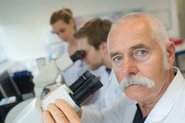 Vědci v laboratoři při pohledu skrz mikroskop čočky — Stock fotografie