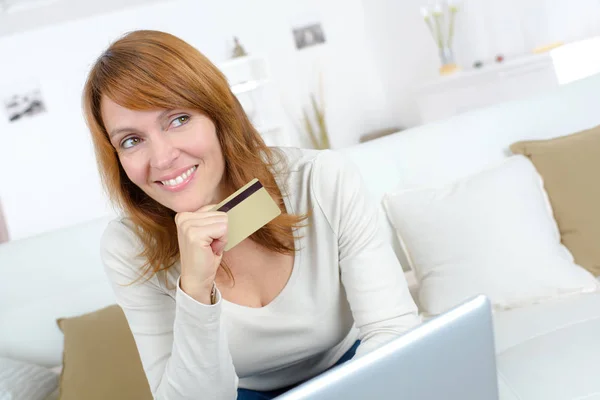 Lächelnde Frau sitzt auf einem Sofa und hält Kreditkarte in der Hand — Stockfoto