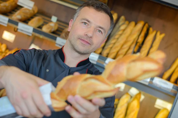 Panadero venta de pan fresco baguettes en panadería —  Fotos de Stock