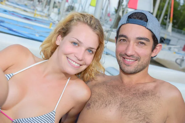 Cheerful couple laying next to sailboats — Stock Photo, Image