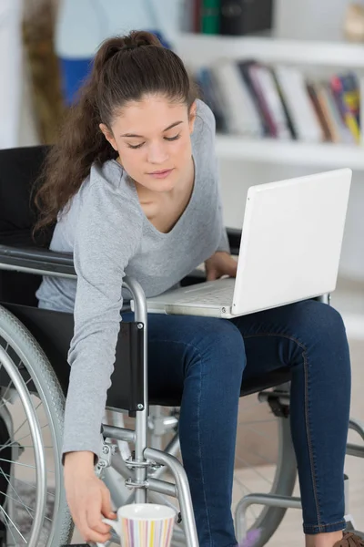 Mulher deficiente segurando uma xícara ao usar seu laptop — Fotografia de Stock