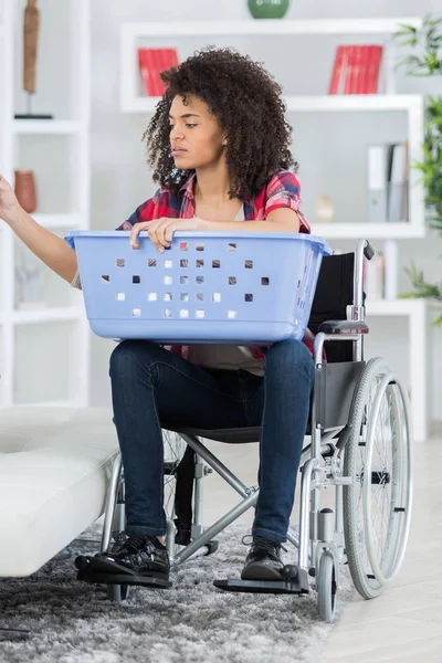 Ung kvinna på rullstolen sätta tvätt i tvättmaskinen — Stockfoto