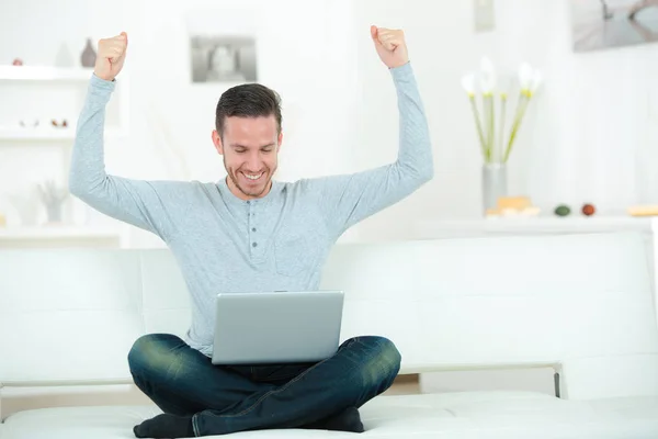 Fröhlicher junger Mann mit Laptop, der drinnen die Hände hebt — Stockfoto