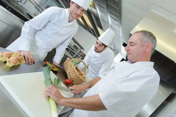 Koch zeigt seinen Assistenten, wie man Gemüse schneidet — Stockfoto