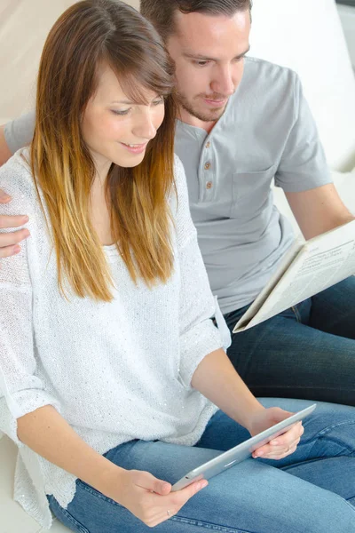 Jeune couple lisant des livres électroniques sur canapé à la maison — Photo