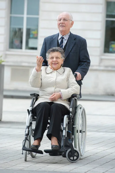 Starší muž tlačí žena na invalidním vozíku ve městě — Stock fotografie