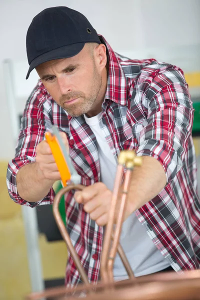 Encanador industrial cortando um tubo de cobre com um cortador de tubos — Fotografia de Stock