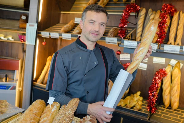 Bäcker steckt Baguette in Papiertüte — Stockfoto