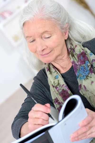 Oude vrouw met een kruiswoordraadsel in de woonkamer Stockfoto