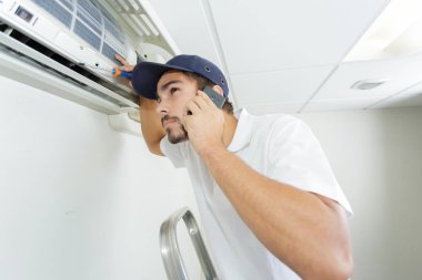 young handyman repairing air conditioning system calling for help clipart