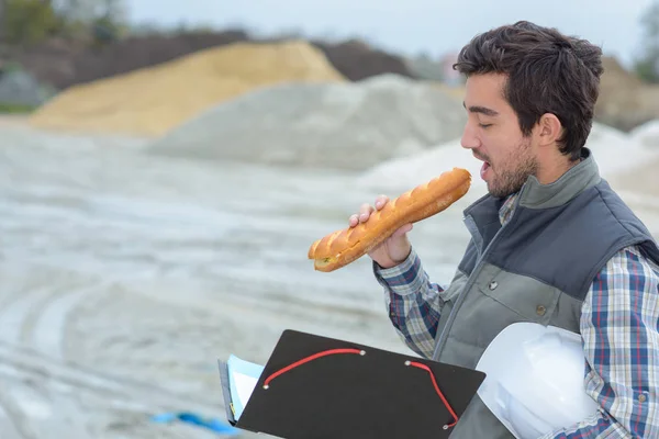 Man eating baguette on building site — Stock Photo, Image