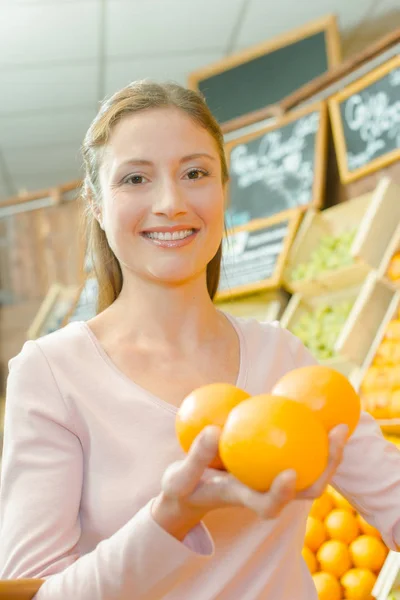 Damen i butiken håller tre apelsiner i hennes hand — Stockfoto