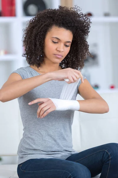 Woman bandaging her wrist indoors — Stock Photo, Image