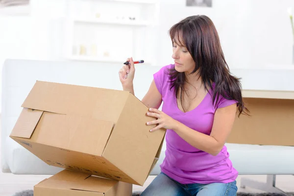 Woman writing with pen on shipping box — Stock Photo, Image