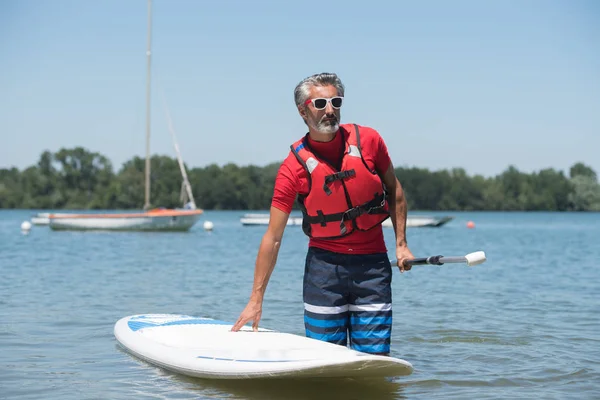 Homem ao lado de um stand-up paddle board no lago — Fotografia de Stock