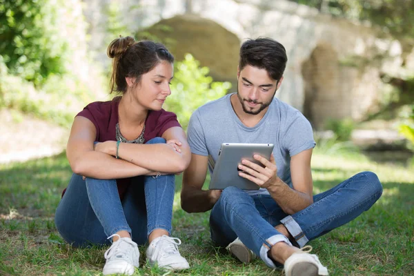 Молодая пара, использующая цифровой планшет в парке — стоковое фото