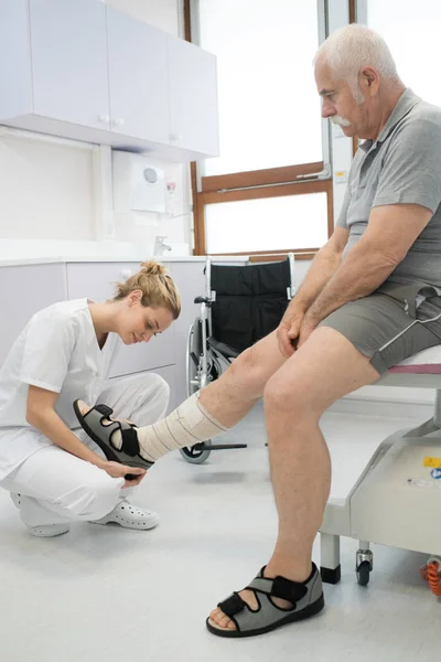 Médecin bandage vieux hommes jambe blessée — Photo