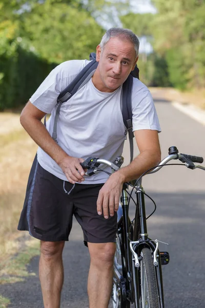 Homem maduro ciclista ao lado de uma bicicleta — Fotografia de Stock