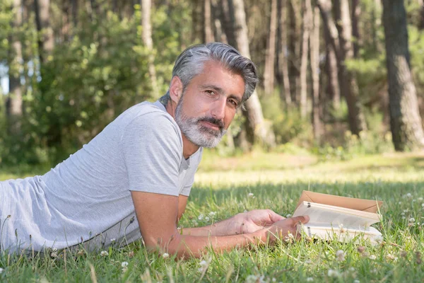 Man lyingsitting in the grass reading a book — Stock Photo, Image