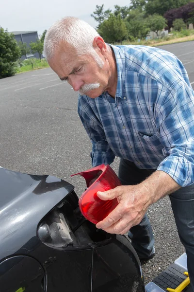 Старик устанавливает задний фонарь на автомобиль — стоковое фото