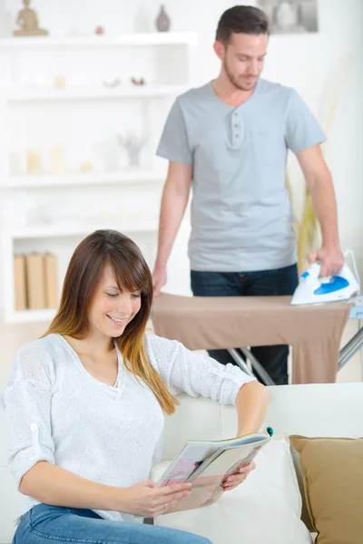 Man ironing while wife reading the news on the sofa — Stock Photo, Image