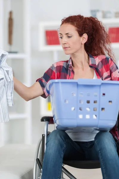 Behinderte Frau sitzt im Rollstuhl und wäscht zu Hause ihre Wäsche — Stockfoto