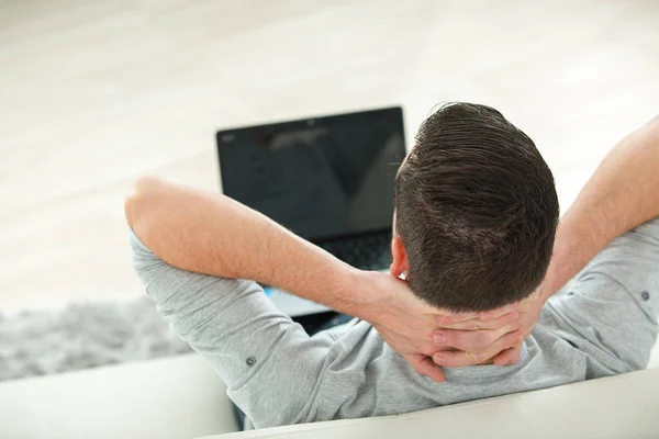 Молодой человек лежит на диване и смотрит видео на ноутбуке — стоковое фото