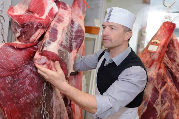 Açougueiro com carcaças e carne — Fotografia de Stock
