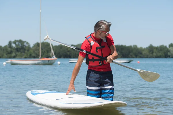 Homem ao lado de um stand-up paddle board no lago — Fotografia de Stock