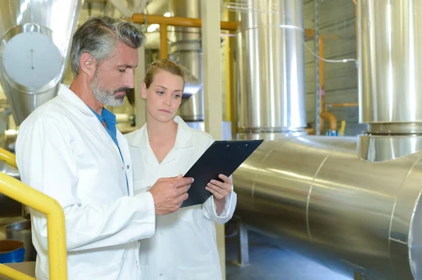 Man and woman in factory holding clipboard — Stock Photo, Image