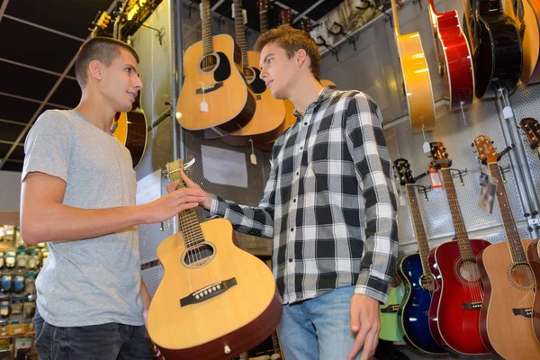 Junge Männer schauen im Geschäft auf die Gitarre — Stockfoto