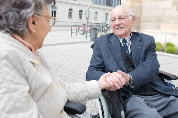 Vieux couple en fauteuil roulant tenant la main à l'extérieur — Photo