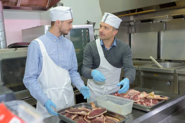 Leerling en chief voorbereiding van vlees in restaurant keuken — Stockfoto