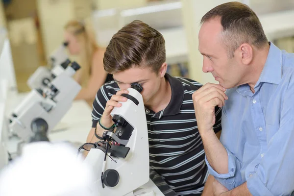 Oglądając spojrzenie student nauczyciel pod mikroskopem — Zdjęcie stockowe