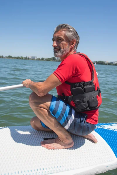 Maduro atraente cavaleiro contemplando natureza sentado no paddle board — Fotografia de Stock