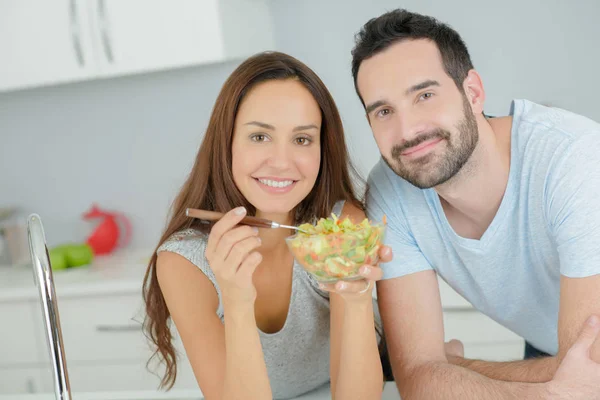 Casal compartilhando uma salada na cozinha — Fotografia de Stock