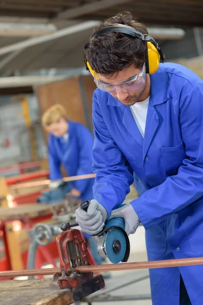 Man angle grinding through copper pipe — Stock Photo, Image