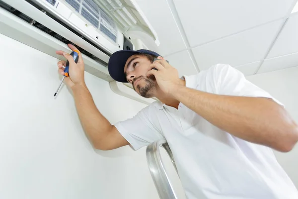 Unga handyman reparerar luftkonditioneringssystem kallar på hjälp — Stockfoto