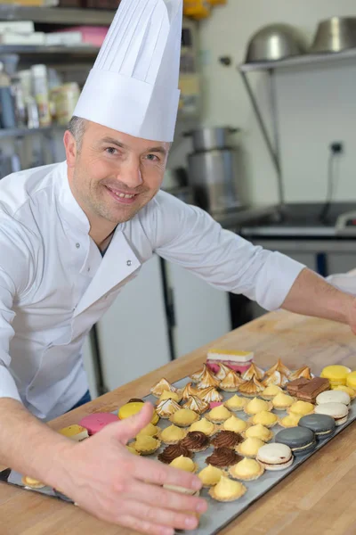 Chef de pastelaria segurando deliciosos bolos e doces — Fotografia de Stock